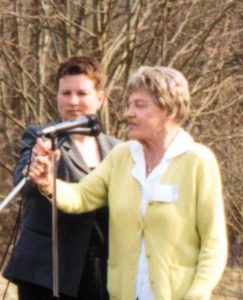 Anita Köcke spricht in ein Mikrofon, neben ihr ist eine weitere Person, dahinter Bäume ohne Blätter.