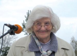 Stanka Krajnc Simoneti, eine alte, lächelnde Frau mit halblangem weißem Haar, spricht in ein Mikrofon